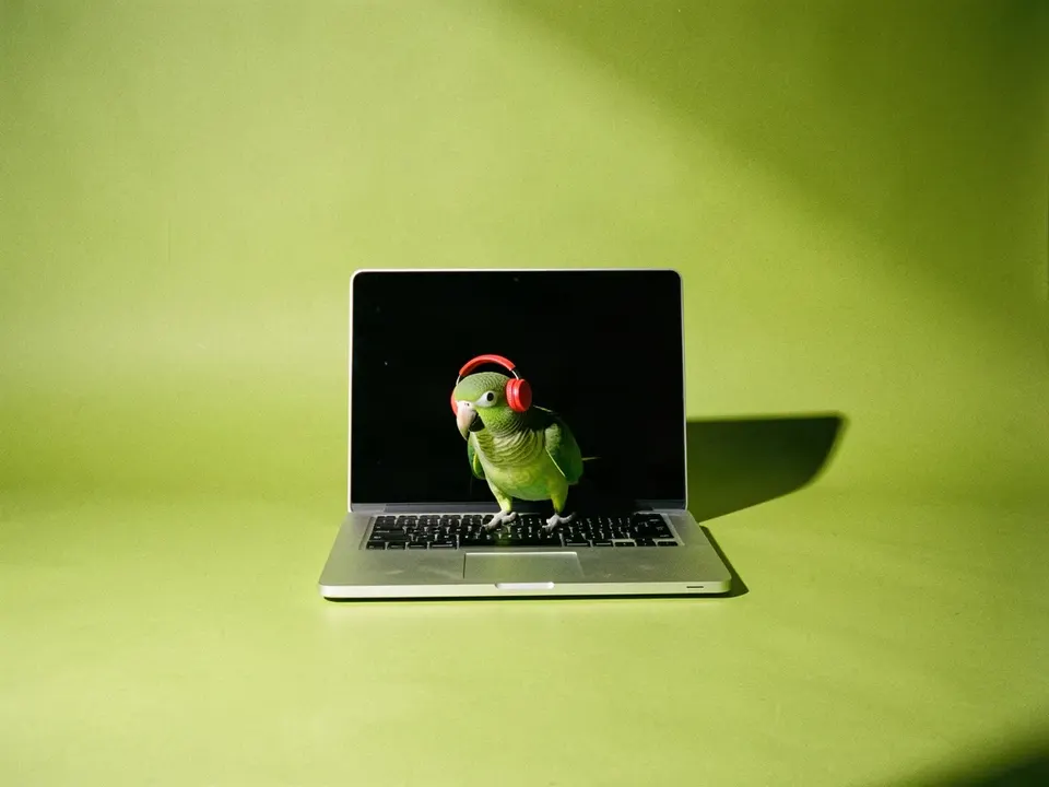 Un loro verde con audífonos rojos frente a una laptop