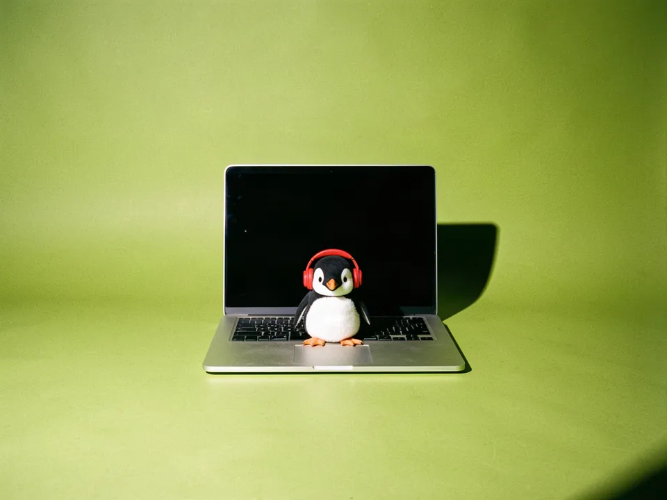 Un pingüino con auriculares sentado frente a una laptop