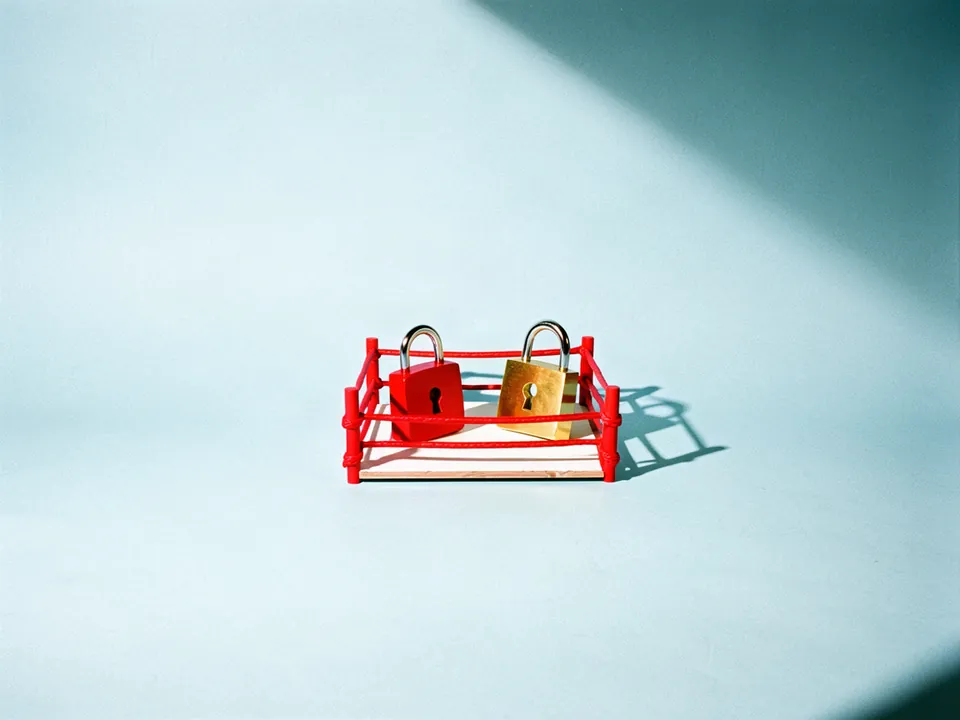 Dos candados, uno rojo y uno dorado, frente a frente en un ring de juguete