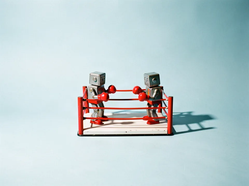 Dos robots de hojalata con guantes de box rojos dentro de un ring de juguete