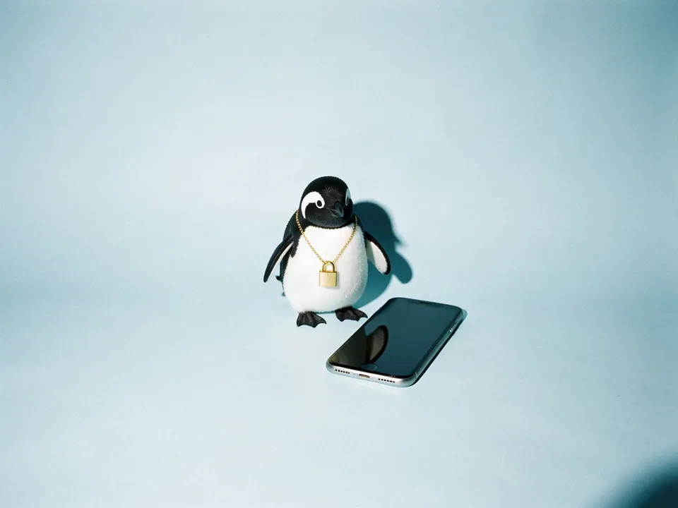 Un pingüino con un candado dorado al cuello junto a un teléfono