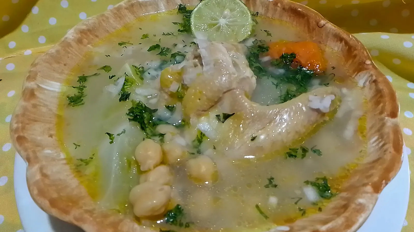 Plato de caldo de pollo con garbanzos, cilantro y una rodaja de limón
