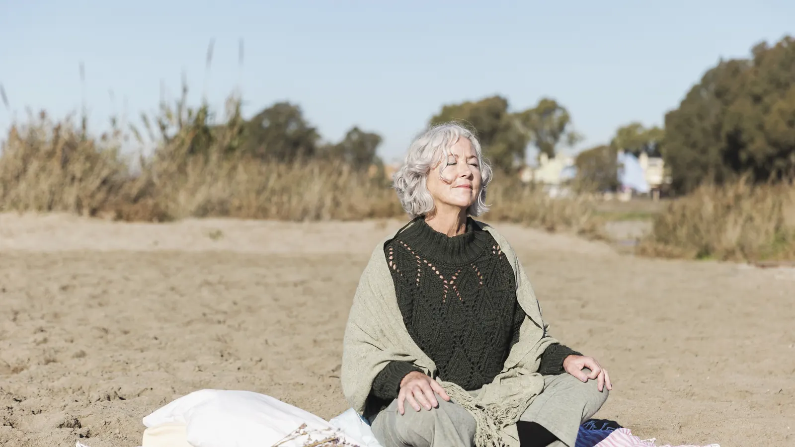 Mujer de cabello canoso sentada con calma al aire libre, sobre la arena