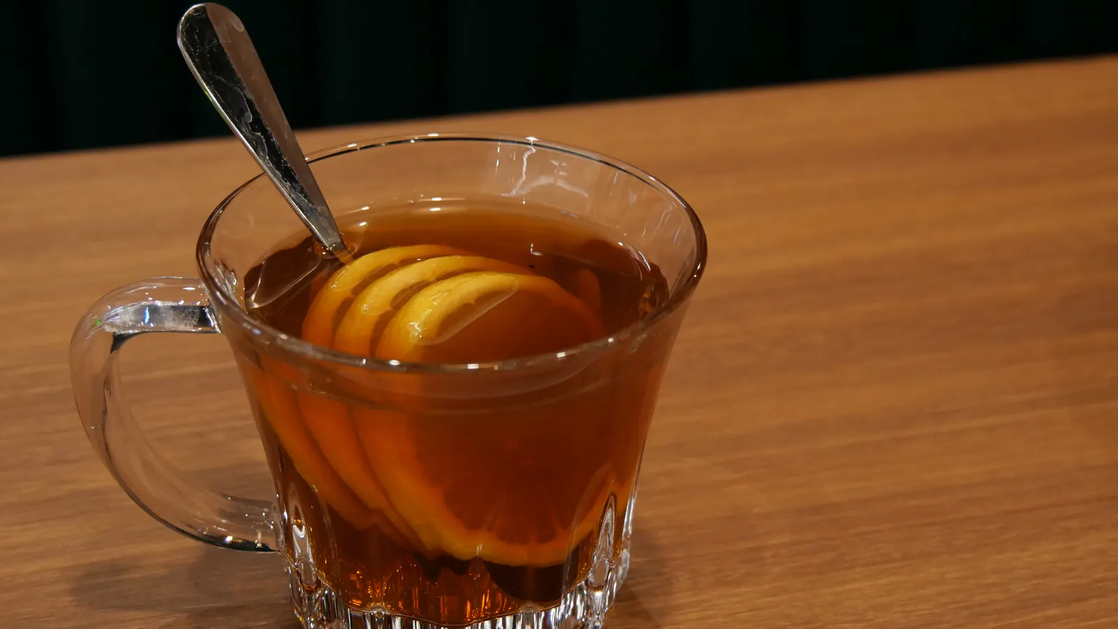 Taza de vidrio con té caliente y rodajas de limón sobre una mesa de madera